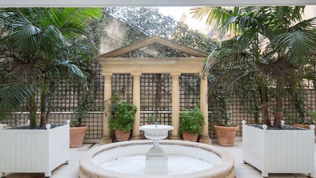 Ein Innenhof mit einer zentralen Fontäne, umgeben von Kübelpflanzen und einer Pergola.