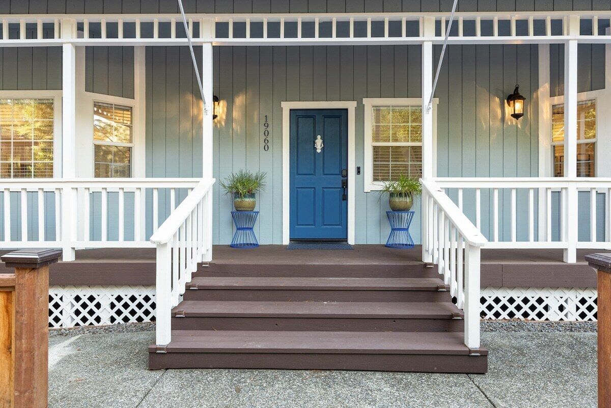 Uma casa de dois andares com uma porta azul na frente, grades brancas e um conjunto de degraus que levam à entrada.