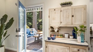A kitchen with white cabinets, a countertop, and a door leading to an outdoor area with a deck and chairs.