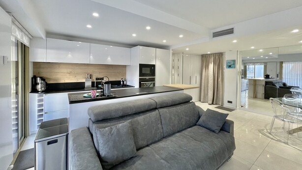 A modern kitchen with white cabinets, a black countertop, and a grey sofa in the living area. - Branly 4, 1 bedroom 50 meters from Croisette parking in etra (Cannes)