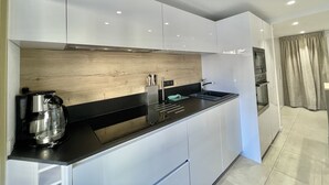 A modern kitchen with white cabinetry, a wooden backsplash, and a black countertop. - Branly 4, 1 bedroom 50 meters from Croisette parking in etra (Cannes)