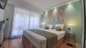 A bedroom with a large bed, a bedside table with a lamp, and a view of the balcony through sheer curtains. - Branly 4, 1 bedroom 50 meters from Croisette parking in etra (Cannes)
