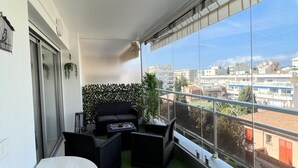 A balcony with a green artificial turf, a white table, black wicker furniture, and a view of buildings.