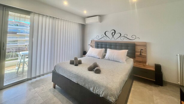A modern bedroom with a large bed, a wooden headboard, and a view of a building through the window.