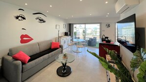 A modern living room with a grey sofa, a glass coffee table, and a dining area with a table and chairs.