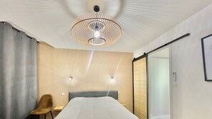 A hotel room with a bed, a desk, a chair, a large window, and a chandelier. - Carre d'or duplex (Cannes)
