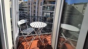 A balcony with a white table and chairs, a metal railing, and a view of multi-story buildings in the background. - Carre d'or duplex (Cannes)