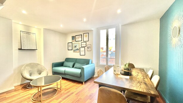 A modern living room with a sofa, a round table, and a dining table. There are framed pictures on the wall and a window with a view. - Carre d'or duplex (Cannes)