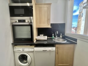 Ett kompakt kök med mikrovågsugn, ugn, diskmaskin och ett fönster med utsikt över en byggnad.