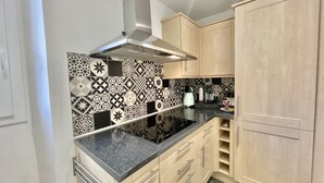 A kitchen with a black and white patterned backsplash, a stainless steel range hood, light wood cabinets, and a black countertop. - Carre d'or duplex (Cannes)