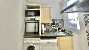 A compact kitchen with a microwave, oven, dishwasher, and a window with a view of buildings. - Carre d'or duplex (Cannes)