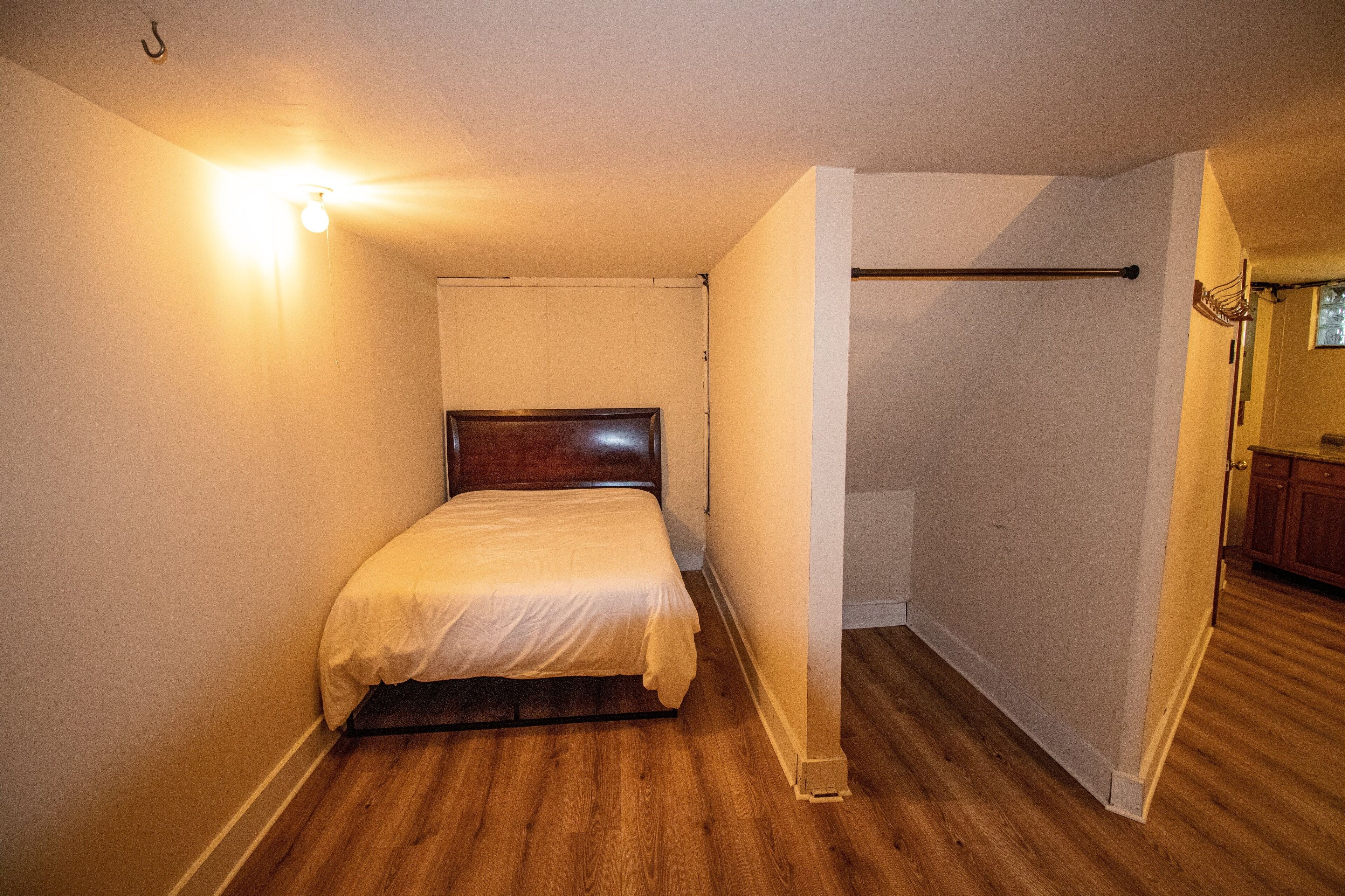 A bedroom with a wooden floor, a single bed, and a light fixture on the wall.