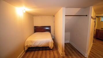 A bedroom with a wooden floor, a single bed, and a light fixture on the wall.