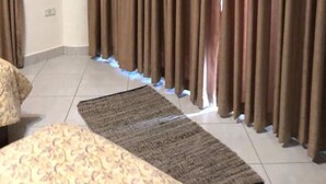 Una habitación con un ventanal grande cubierto por cortinas marrones, un sofá estampado y una alfombra oscura en el suelo.