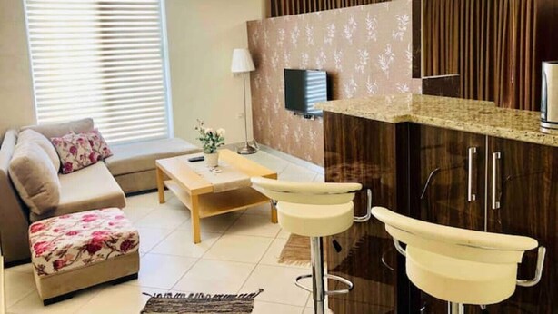 Una sala moderna con un sofá, una mesa de centro y un televisor. Cuenta con una zona de cocina con una encimera y un lavabo.