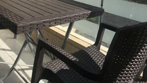 Een balkon met glazen hekwerk, een tafel en twee rieten stoelen.