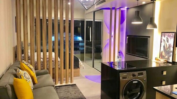 Een moderne woonkamer met een bank, kussens, een wasmachine en een glazen scheidingswand.