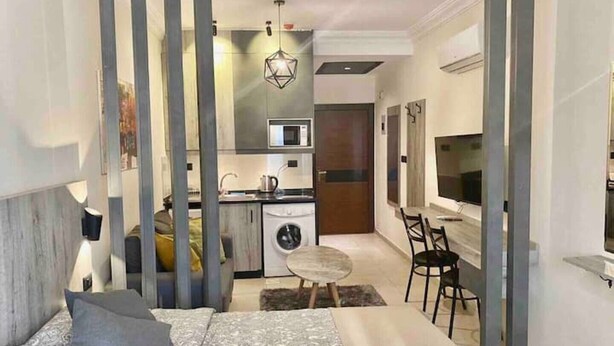 A modern bedroom with a bed, bedside table, and a view of a compact kitchenette.