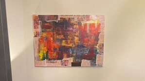 A gray sofa with four cushions in a room with a large abstract painting on the wall.