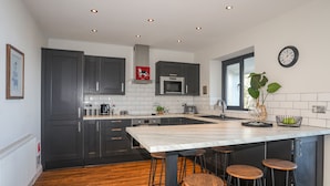 A modern kitchen with dark cabinets, a large island with stools, a microwave, and a clock on the wall.