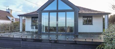 Een modern huis met een grote glazen voorgevel, een schuin dak en een houten terras.