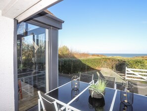 Un espace de restauration extérieur moderne, avec une table et des chaises en verre, une plante en pot et une vue sur la mer.