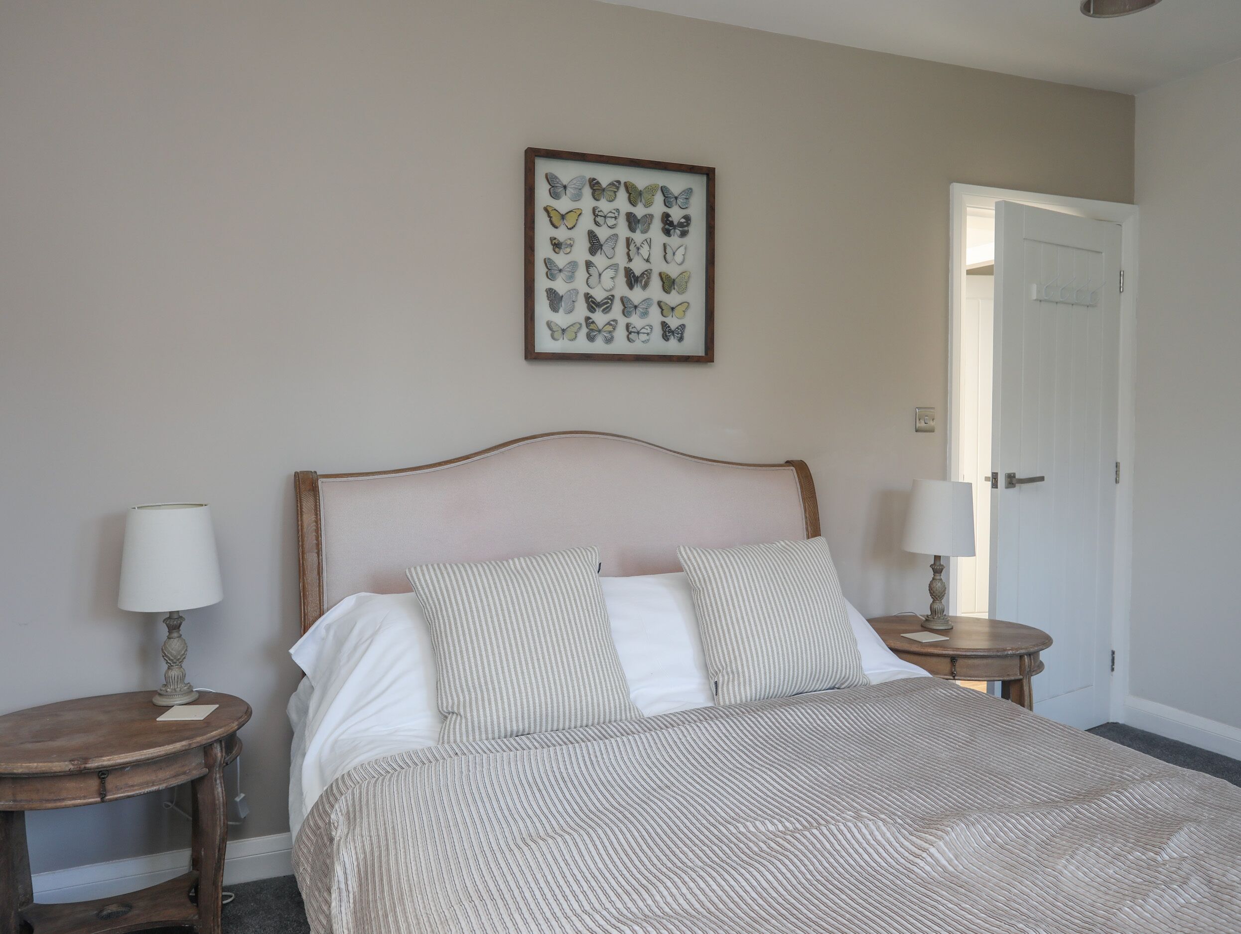 Een slaapkamer met een bed, twee nachtkastjes, een vlinderkunstwerk in een lijst en een deur.