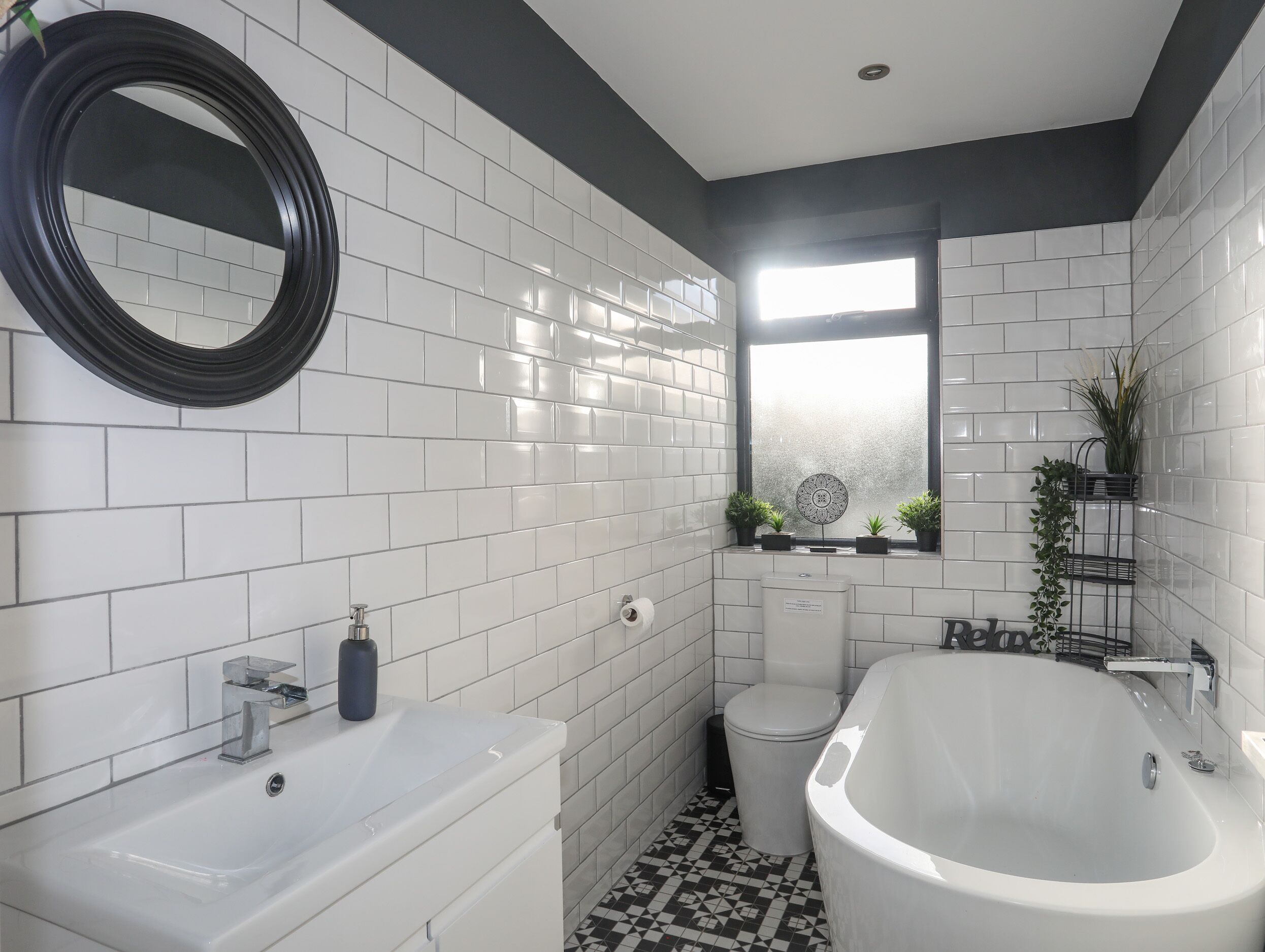 Un baño moderno con azulejos blancos tipo metro, una bañera grande, un inodoro y un lavabo.