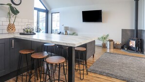 A modern kitchen with a marble countertop, black stools, a built-in TV, and a wood-burning stove.