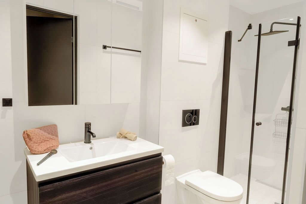 A modern bathroom with a white sink, dark wood vanity, a glass shower enclosure, and a toilet.