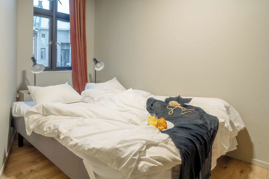 Ein ordentlich bezogenes Bett mit weißer Bettwäsche, eine Schere und ein Croissant auf einem Teller.