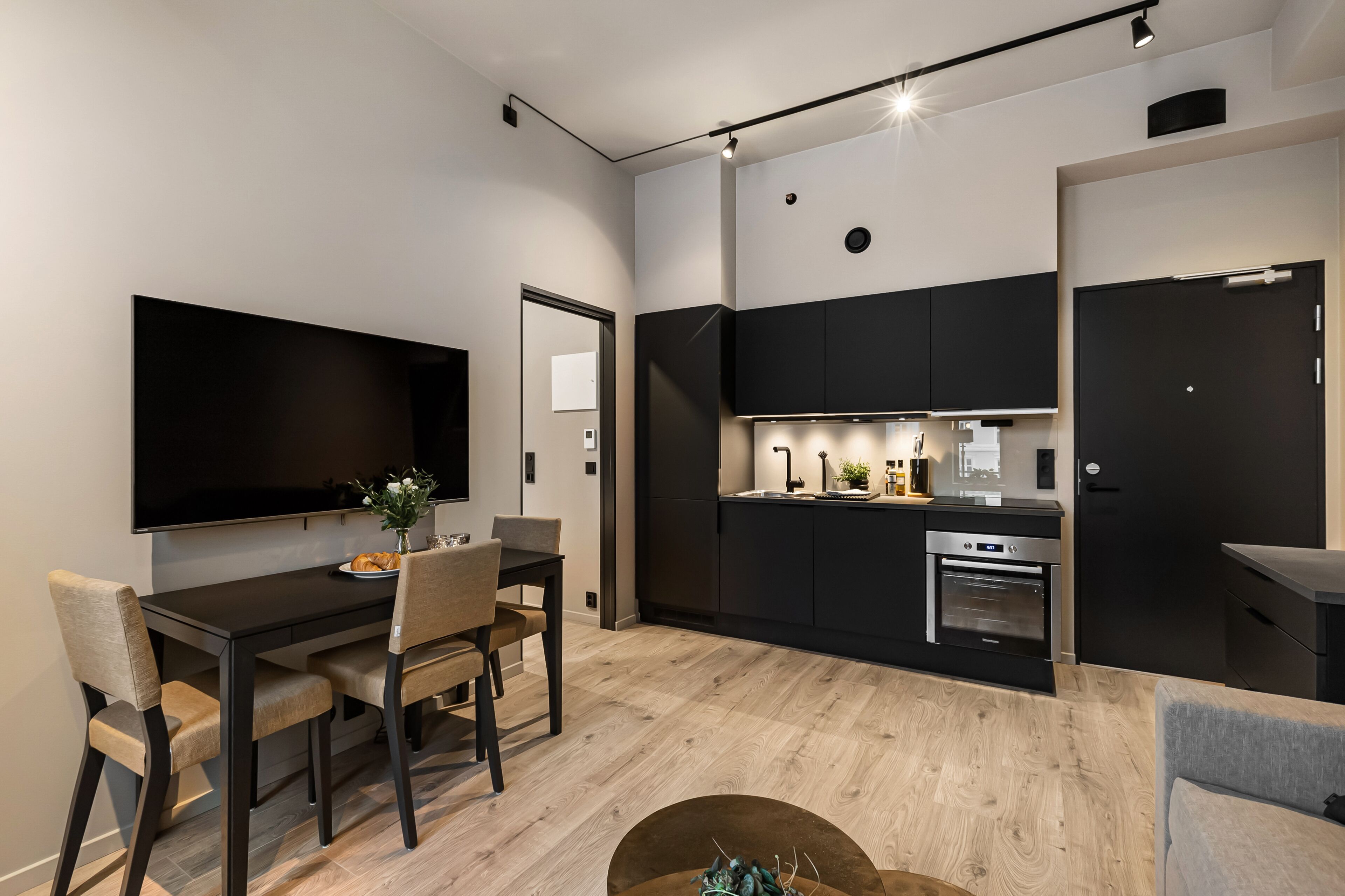 A modern kitchen with black cabinets, a built-in oven, and a dining area with a table and chairs.