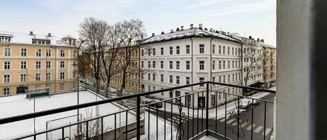 A balcony with a metal railing overlooking a snow-covered street and buildings.