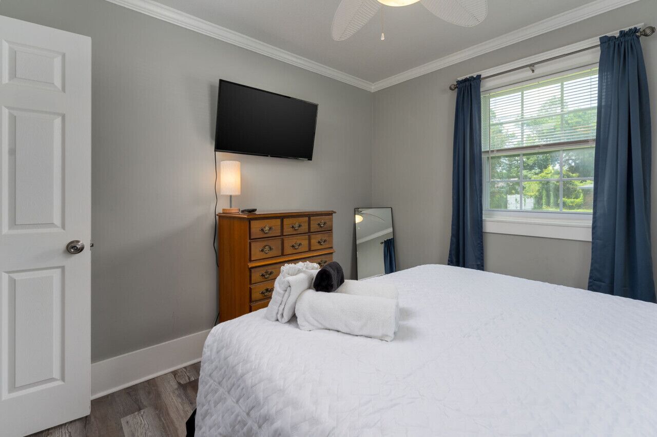 Een hotelkamer met een bed, een dressoir, een televisie, een raam met gordijnen en een deur.