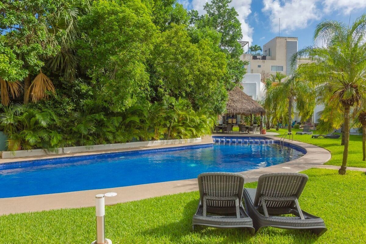 A swimming pool with lounge chairs, surrounded by lush greenery and a thatched-roof structure.