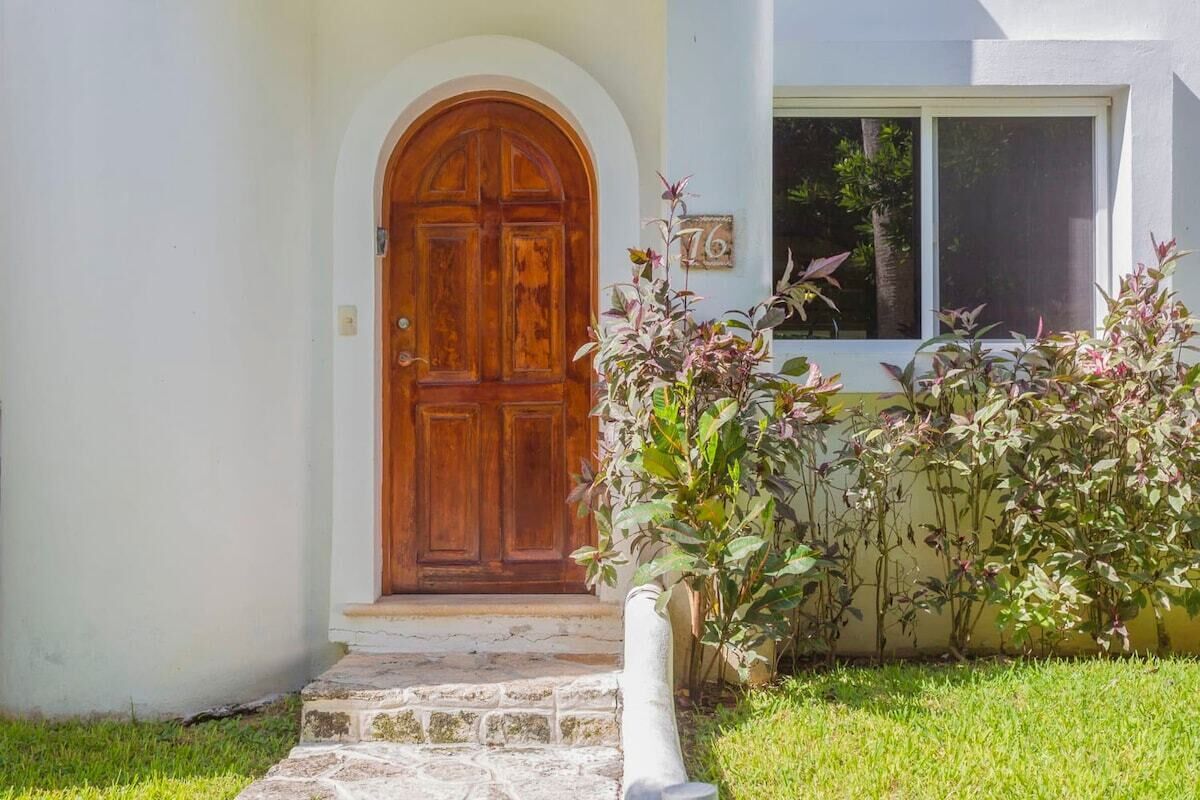 Una casa con puerta de madera, una escalera de piedra y un cartel con el número 76 en la pared.