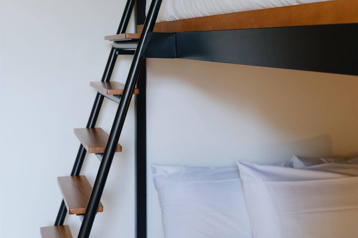 A bunk bed with a wooden ladder and white bedding.