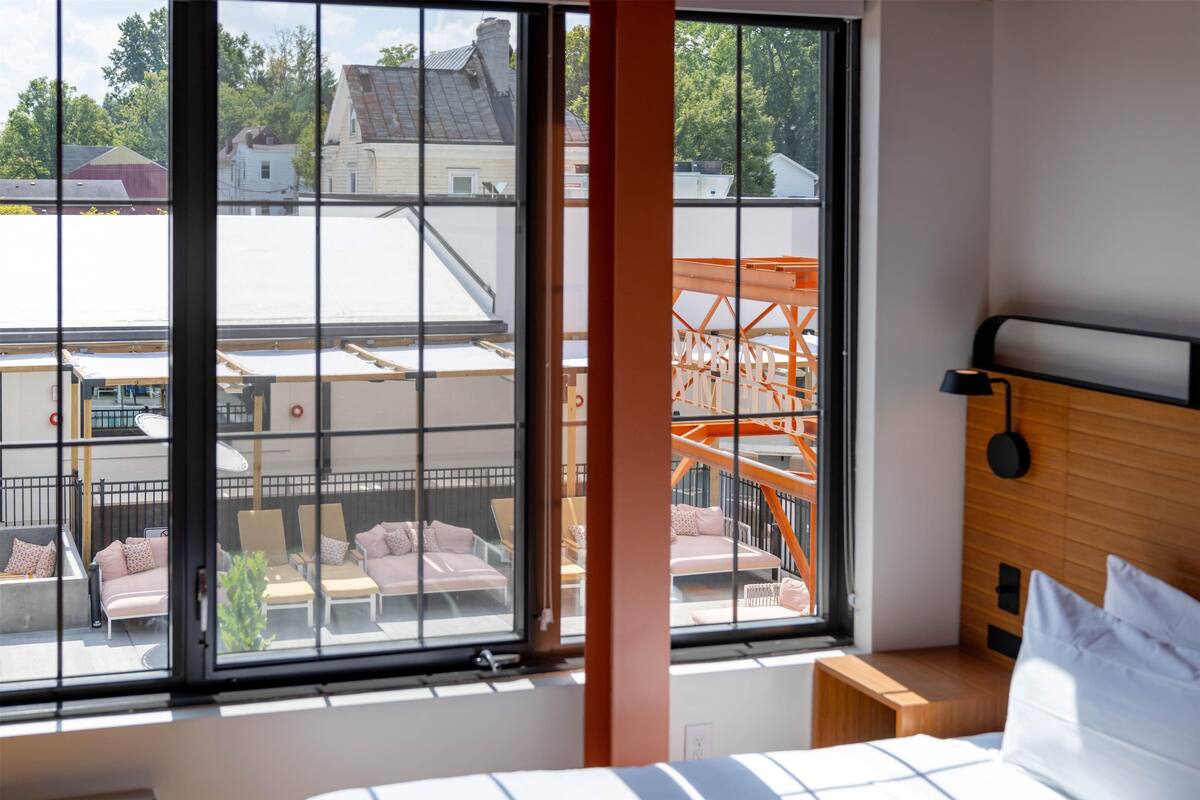 A hotel room with large windows, a bed, a nightstand, and a view of the outside.