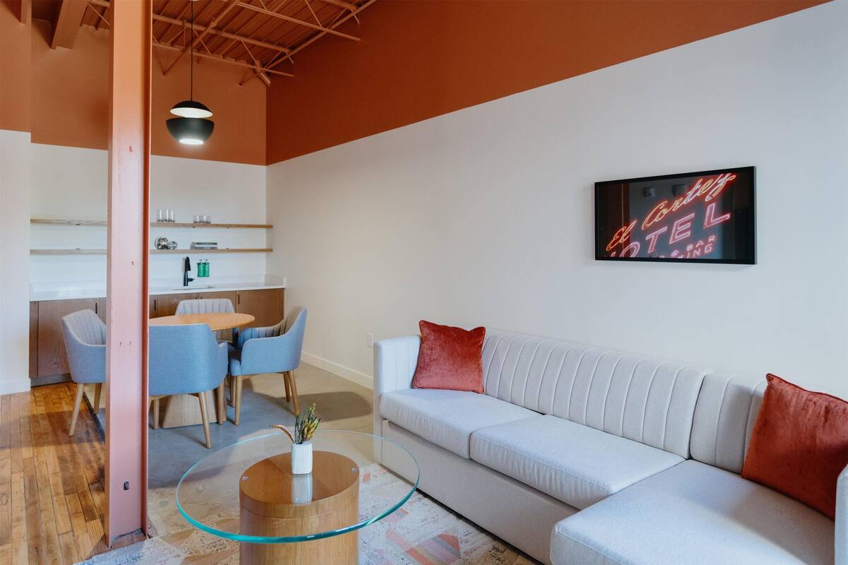 A modern living room with a white sofa, glass coffee table, and a dining area with chairs and a table.