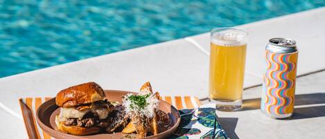 Un plato con una hamburguesa y papas fritas, una jarra de cerveza y una lata al lado de una piscina.
