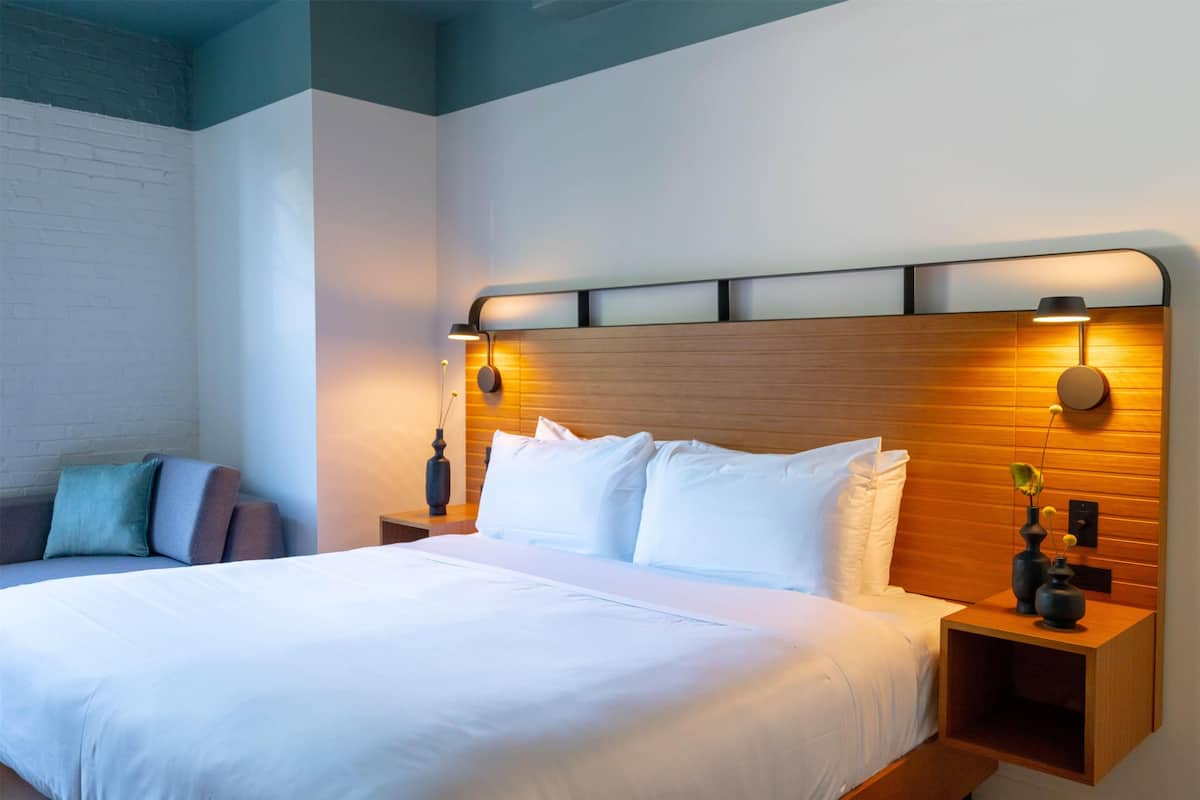 A modern hotel room with a large bed, wooden headboard, and bedside lamps.