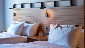 A hotel room with two beds, each with white linens and pillows. There is a wooden headboard with built-in lighting and a small potted plant on the nightstand.