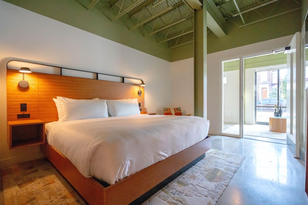 A modern bedroom with a wooden headboard, a large bed, and a view through a glass door.