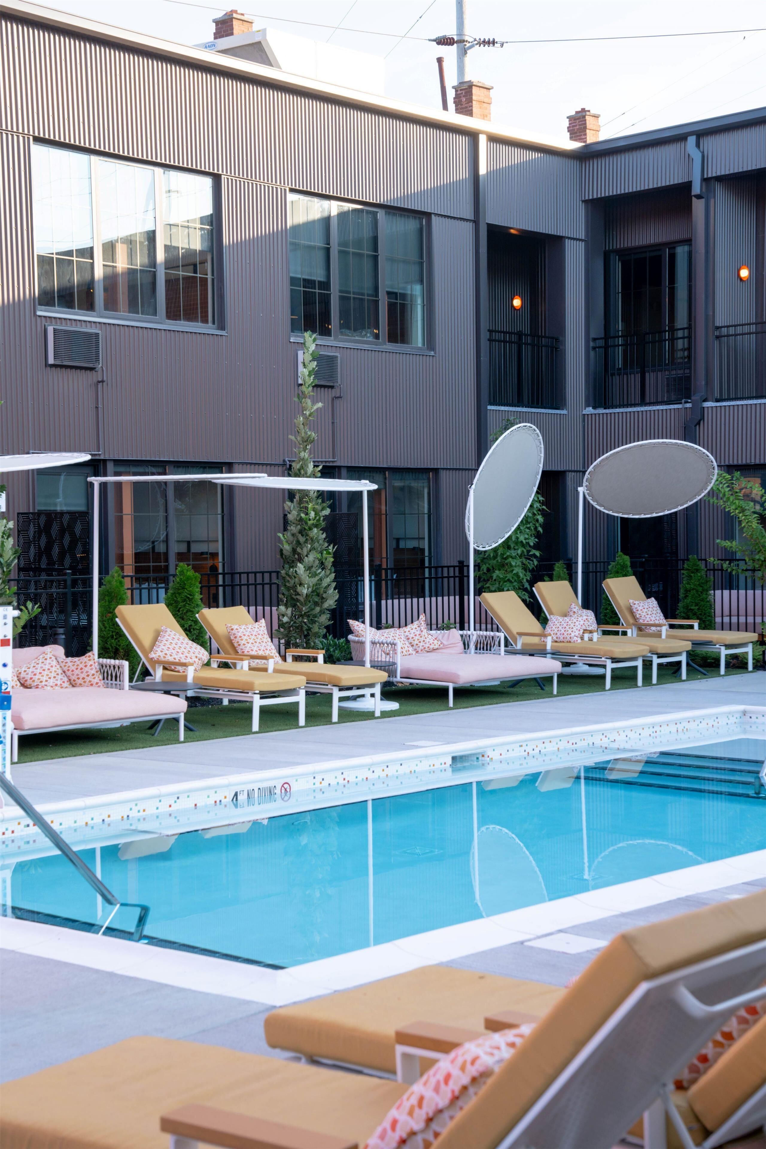 A modern building with a swimming pool, sun loungers, and a covered seating area.