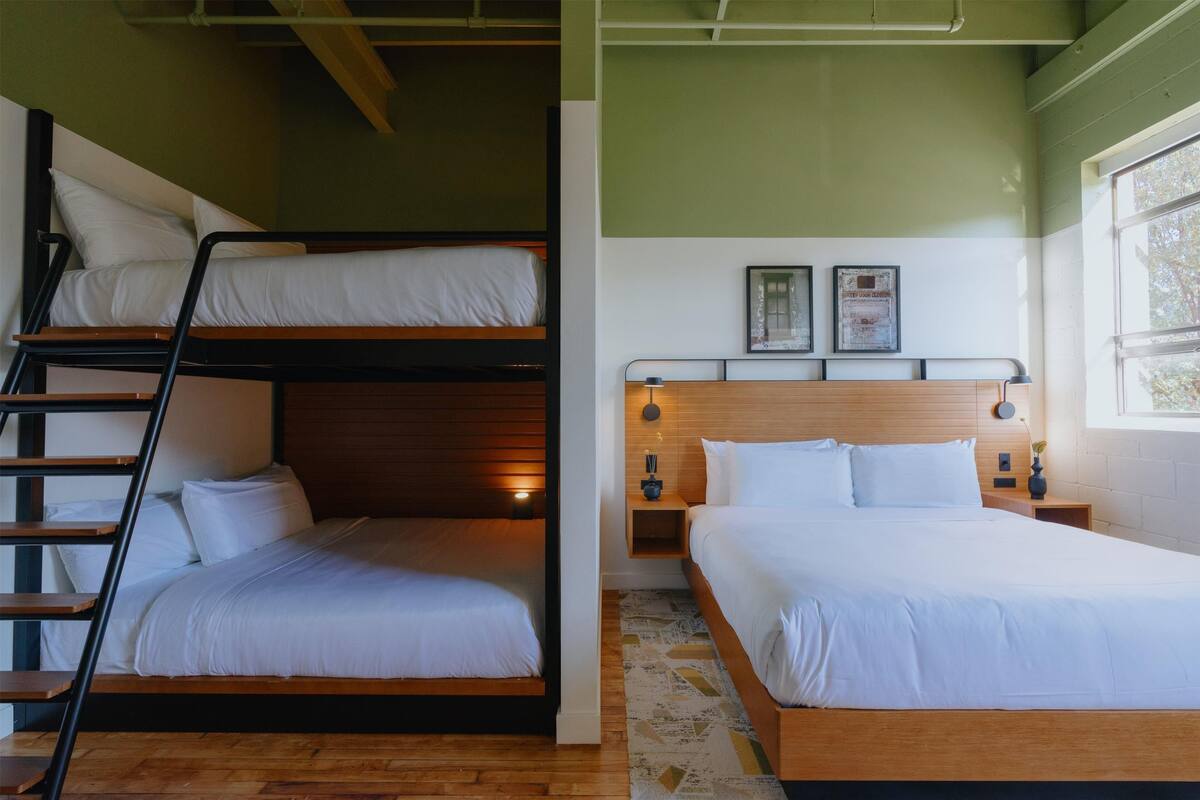 A room with bunk beds, a wooden headboard, a nightstand, and a window with natural light.