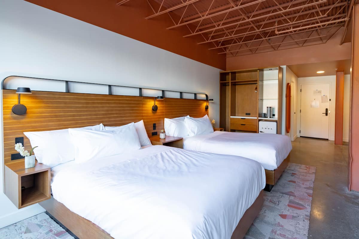 A hotel room with two beds, wooden headboards, and a modern design.