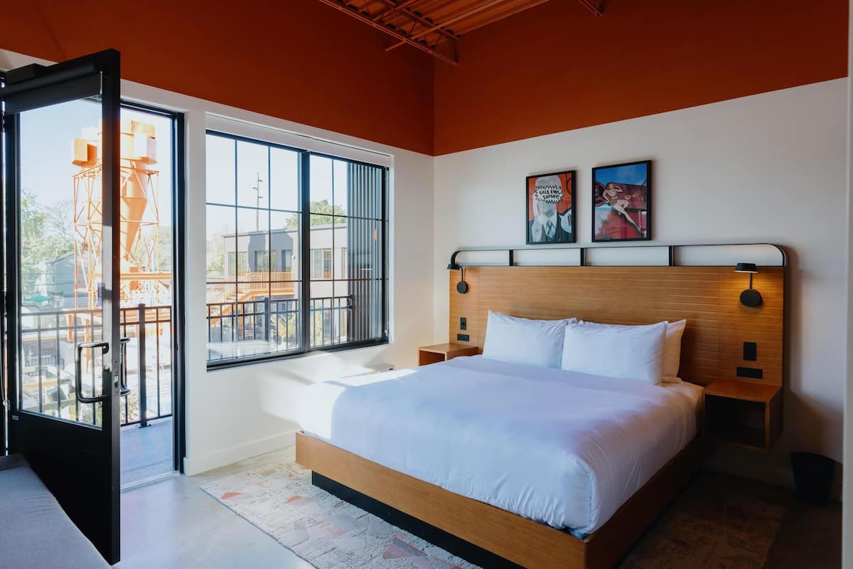 A modern bedroom with a large bed, a window with a view of a construction site, and two wall-mounted artworks.