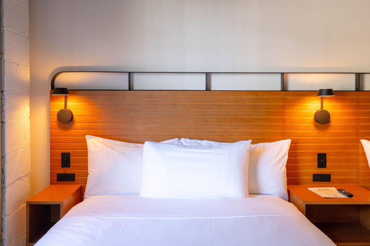 A hotel room with a wooden headboard, two bedside tables, and a bed with white linens.