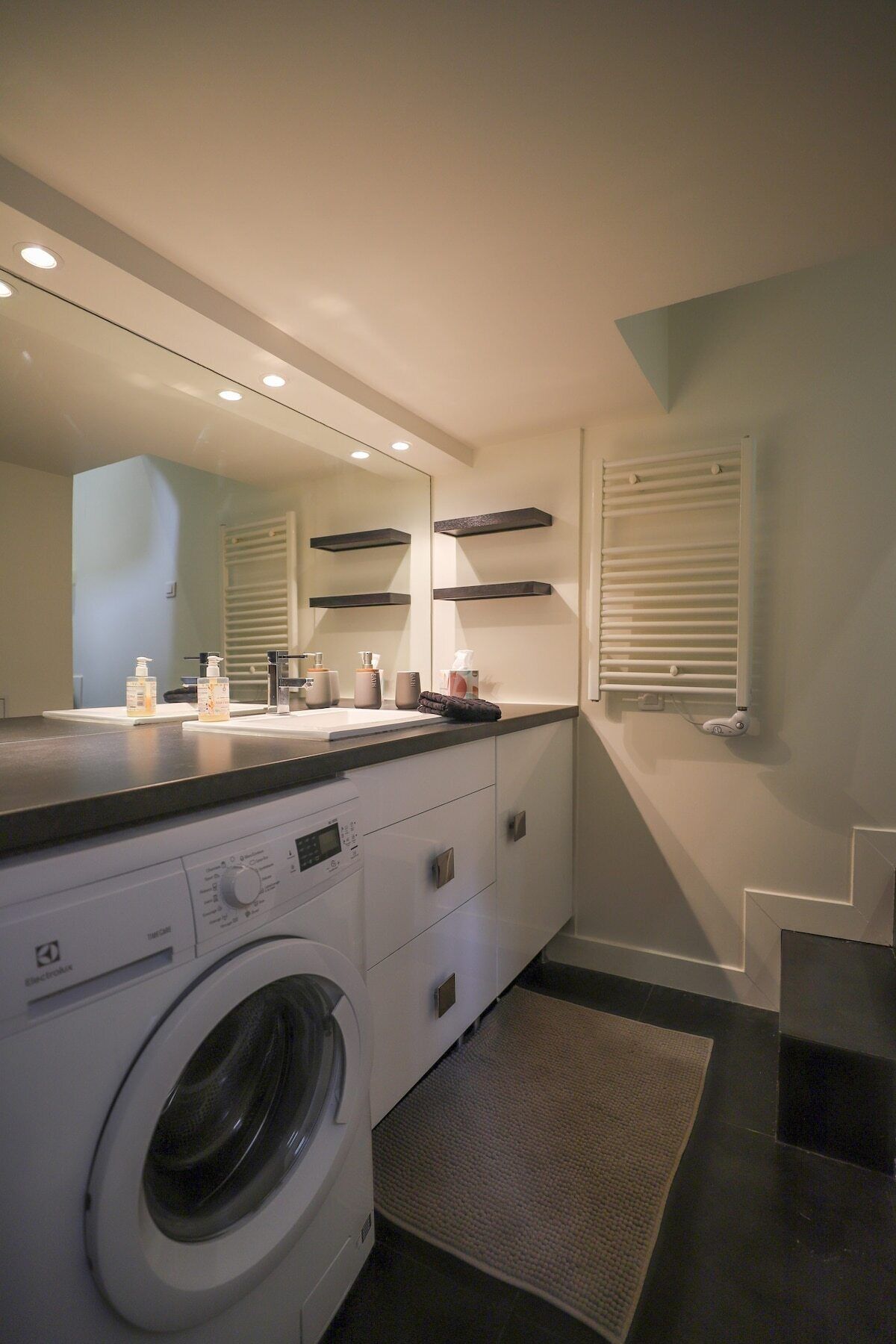 Un baño moderno con lavadora incorporada, un espejo grande y una encimera con artículos de aseo.
