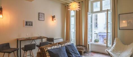 A cozy room with a bed, a desk, and chairs. There is a window with curtains and a view of the outside.